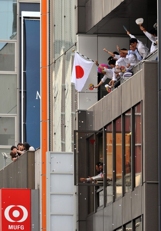 Workers wave from their offices as they watch Japan's medallists фото