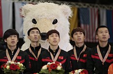 Конькобежный спорт A championship mascot stands behind Chinese team members as they фото (photo)