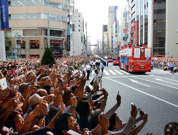Crowds of people wave to Japan's Olympic medallists riding фото